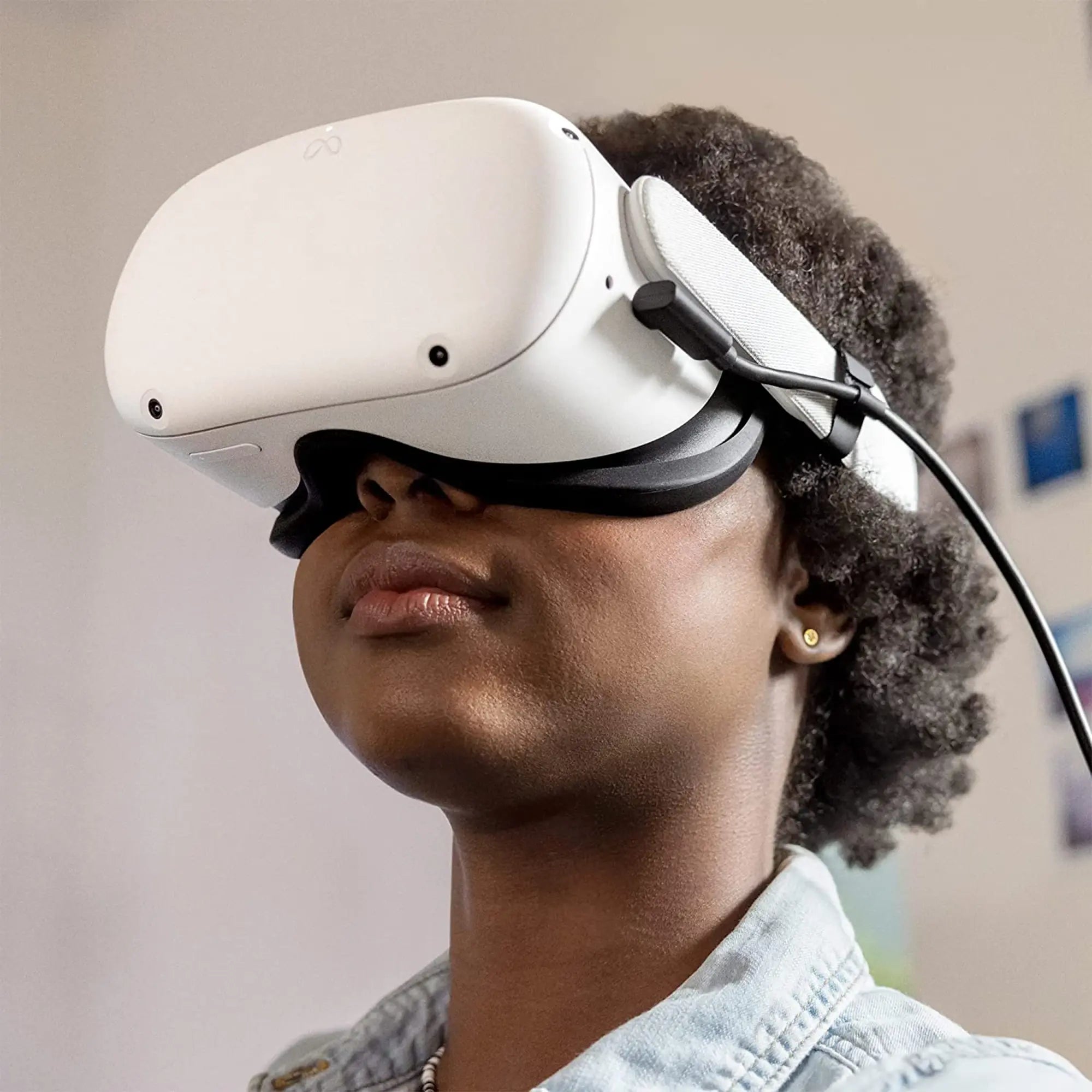 A person wearing a white virtual reality headset with a black strap. They have short curly hair and are wearing a light blue shirt. The background is blurry, focusing on the individual immersed in their VR gaming experience, showcasing essential VR accessories.